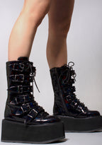 Demonia DAMNED 225 Necromancer Hologram Black Platform Boots in iridescent holographic vegan leather with cone studded straps and lace-up front worn by model — side view