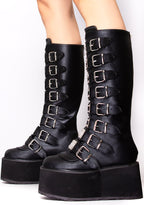 Demonia DAMNED 318 Obsession Black Platform Boots in black vegan leather with buckle strap front and traction sole worn by model — side view