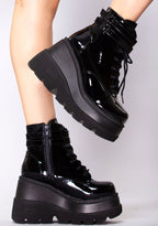 Demonia SHAKER 52 Paint it Black Patent Black Platform Boots in black patent leather with strap buckle front and lace-up closure worn by model — side view
