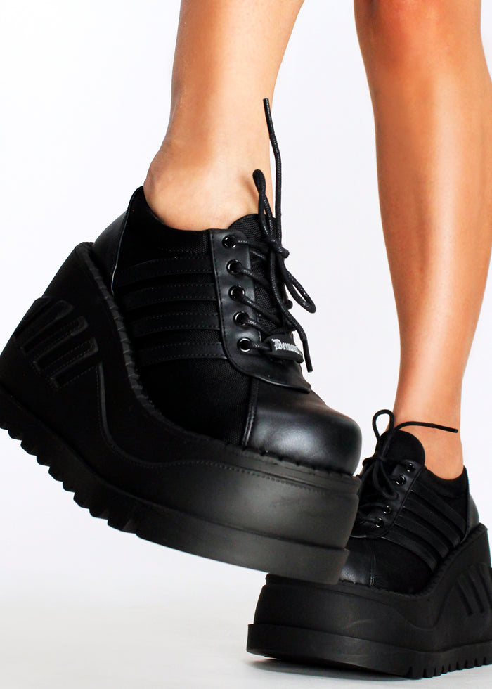 Demonia STOMP 08 Black Rave Platform Sneakers in black vegan leather with lace-up closure and chunky rubber platform worn by model — side view