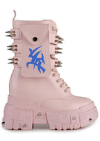 Side studio profile of Anthony Wang X WTF CV Chem Baby Metal Pink platform boots showing the pastel pink faux leather upper, utility side pocket with blue tribal symbol graphic, and spiked chunky platform soles